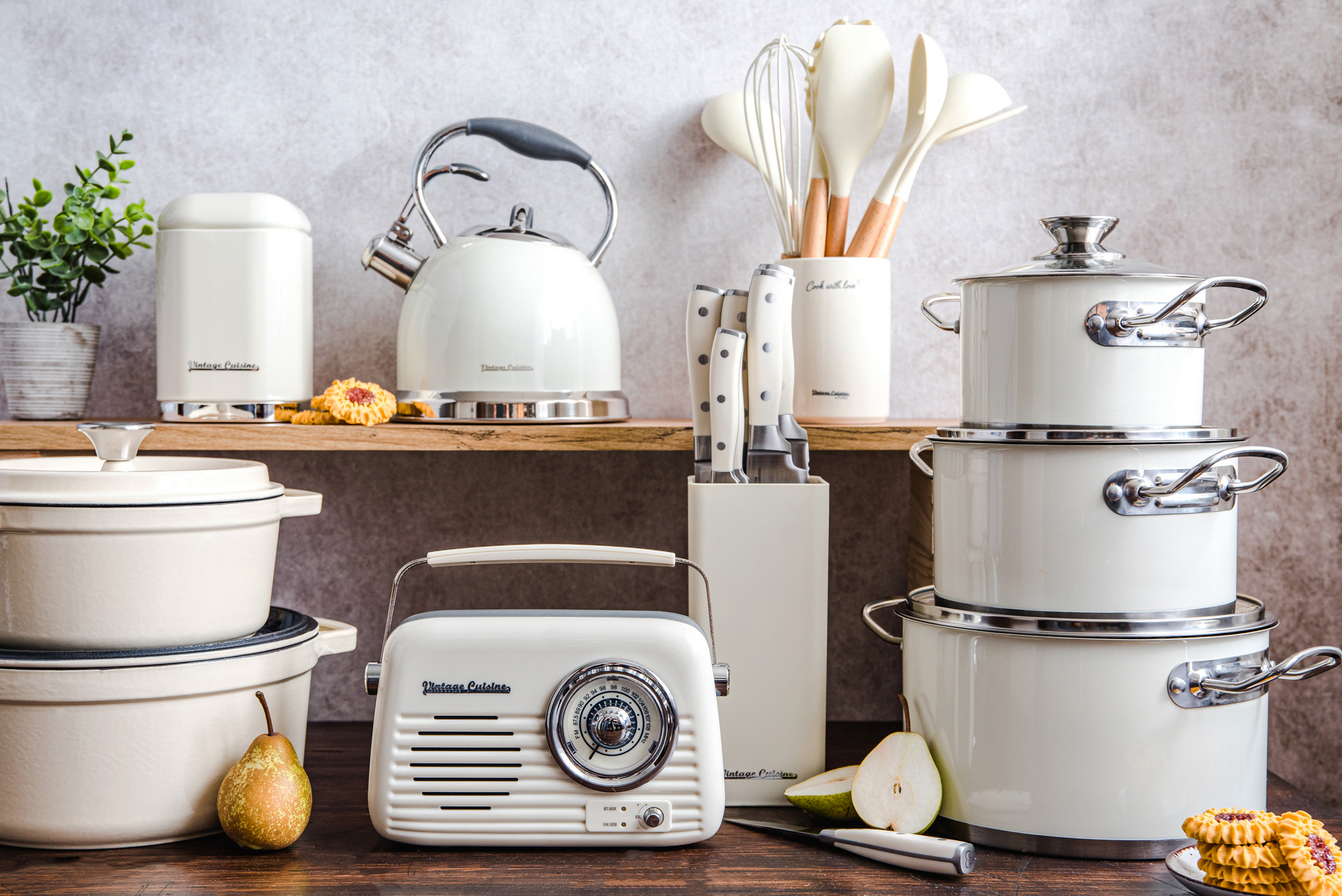 Produkty Vintage Cuisine w kremowym kolorze. Na pierwszym planie radio, obok garnki żeliwne i emaliowane, a na półce czajnik, pojemnik i akcesoria kuchenne.