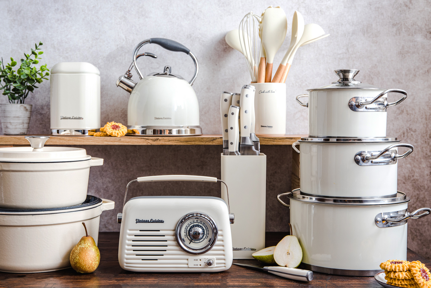 Produkty Vintage Cuisine w kremowym kolorze. Na pierwszym planie radio, obok garnki żeliwne i emaliowane, a na półce czajnik, pojemnik i akcesoria kuchenne.