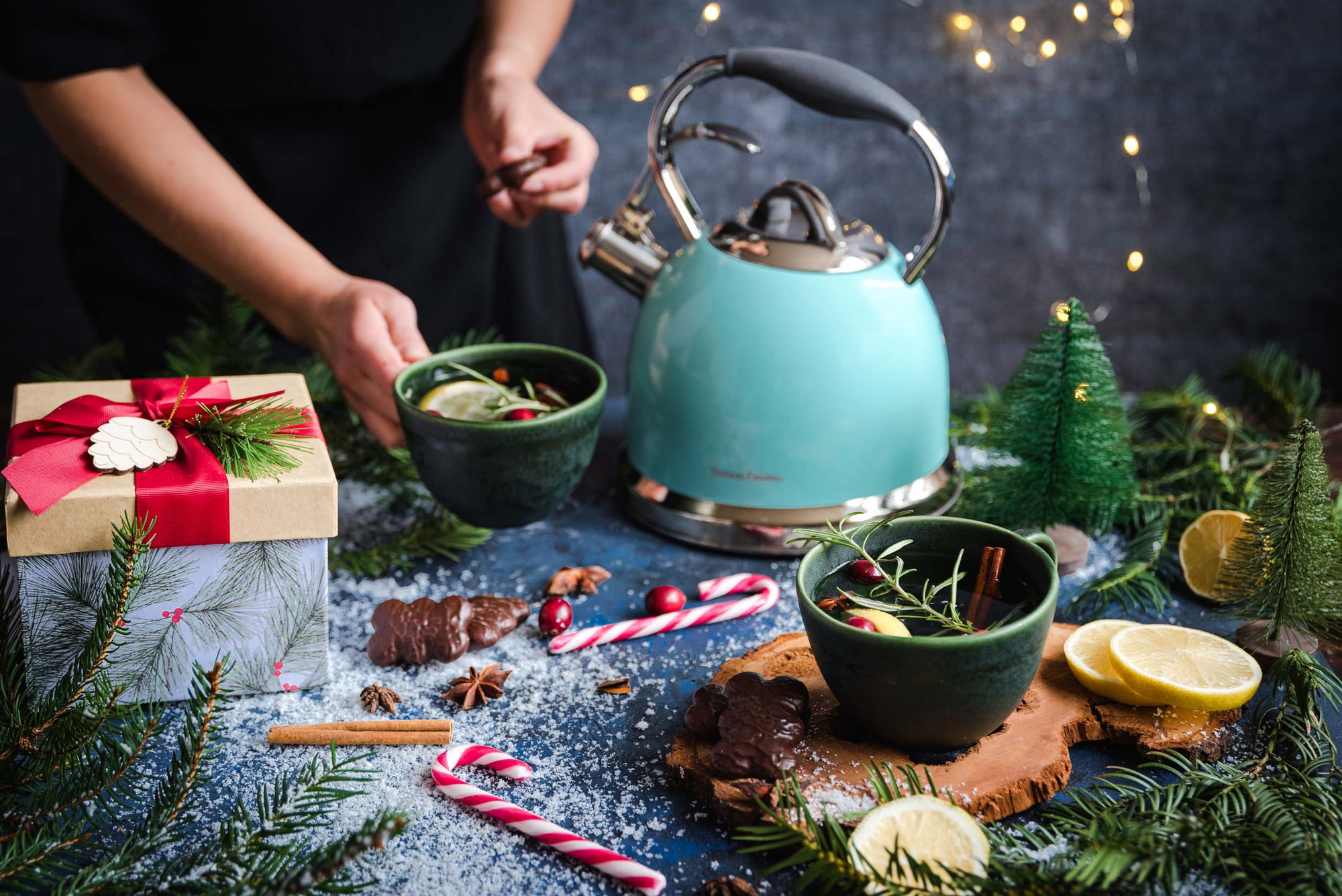 Turkusowy czajnik elektryczny w stylu retro na świątecznym stole w otoczeniu zimowej herbaty, prezentu i dekoracji bożonarodzeniowych.